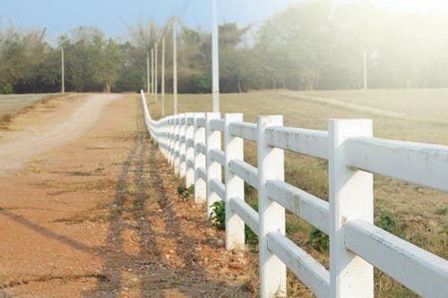 White ranch rail fence receding along a sunlit Virginia country lane