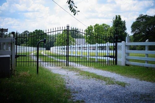 White ranch rail fence lining a driveway entrance under a clear Virginia sky